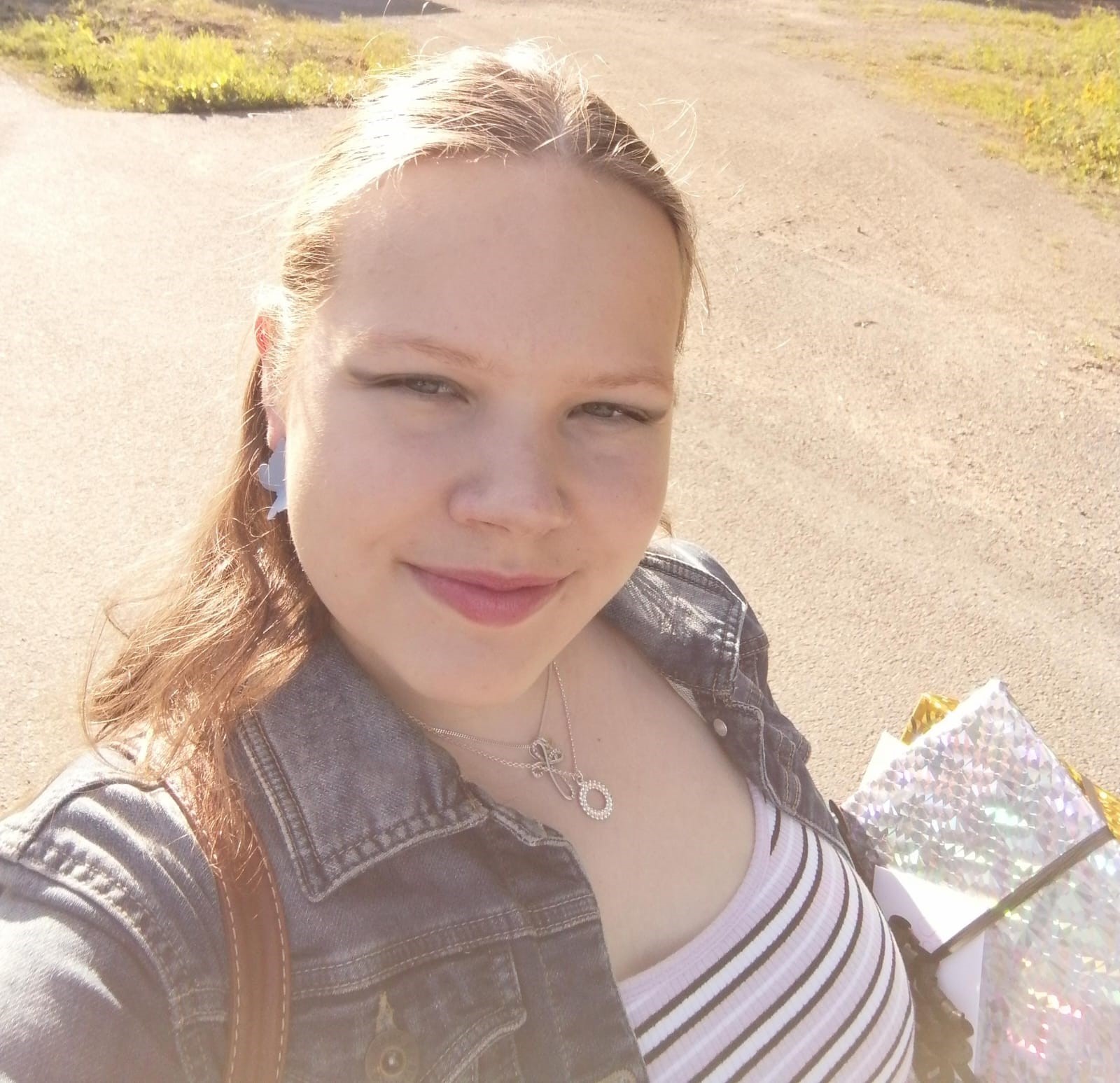 Annika, valkoinen nainen ottaa selfietä. Hän seisoo aurinkoisella tiellä hymyillen ja hänellä on pitkät vaaleat hiukset.