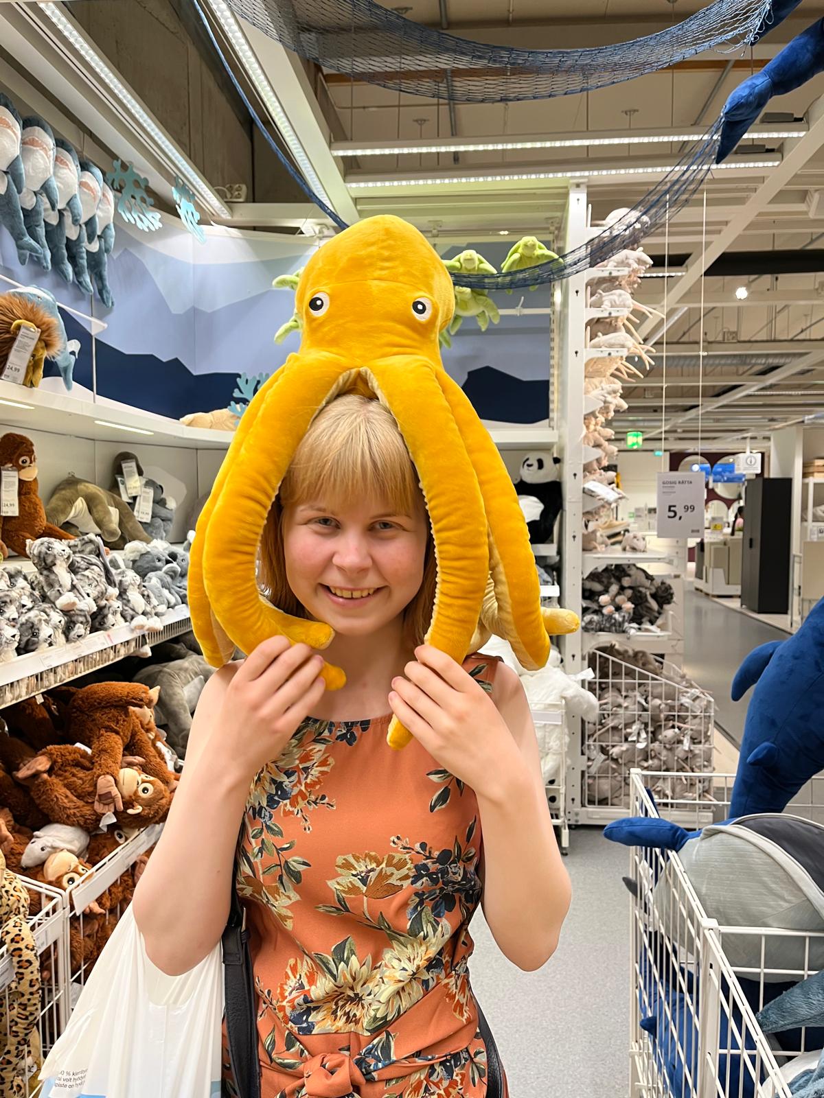 Kiona istuu heinäpellossa päällään punainen pitkähihainen mekko ja musta liivi. Hän kurottaa kädellään kohti aurinkoa ja varjo osuu hänen kasvoihinsa. Hänellä on vaalea, ruskea iho ja mustat, kiharat hiukset joiden latvat on värjätty vaaleaksi.